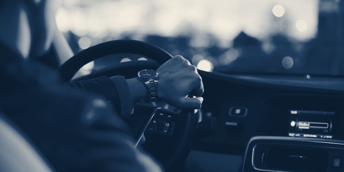 Mãos no volante de um carro em via urbana